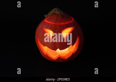 Close-up on a Jack O' Lantern lit in the dark and reflecting on a black surface in front of it. Stock Photo