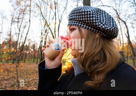 Ukraine. Sunset. City Park. End of the working day. A girl drinks coffee from a cup with a patriotic sticker "I love Ukraine". Walks in the open air Stock Photo