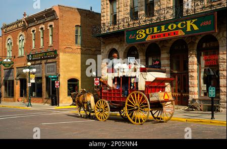 An old-fashioned stagecoach carries tourists past the old Bullock Hotel on Main St. in the Black Hills gold rush town of Deadwood, South Dakota. Stock Photo