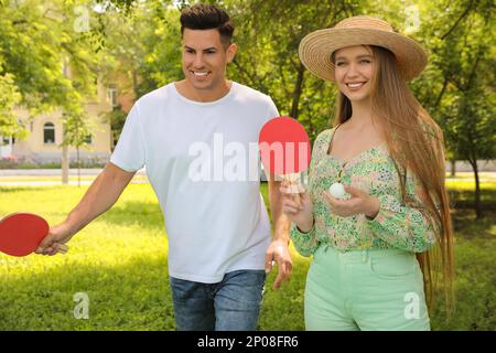 Happy couple with tennis rackets and ball near ping pong table in park Stock Photo