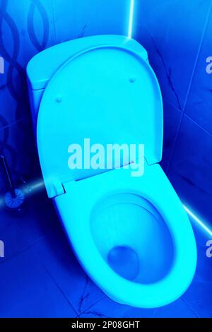 Toilet bowl in public restroom lit with UV blue light Stock Photo