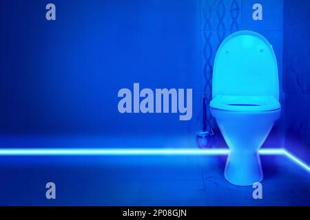 Toilet bowl in public restroom lit with UV blue light Stock Photo