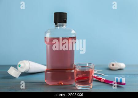 Bottle and glass with mouthwash near other oral hygiene products on light blue wooden table Stock Photo
