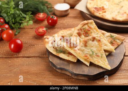 Cut delicious khachapuri with cheese, dill and tomatoes on wooden table Stock Photo