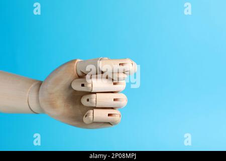 Wooden mannequin hand showing fig sign on light blue background. Space for text Stock Photo