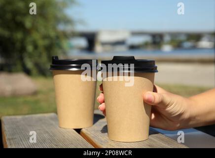 Woman taking cardboard coffee cup with plastic lid at wooden table outdoors, closeup Stock Photo