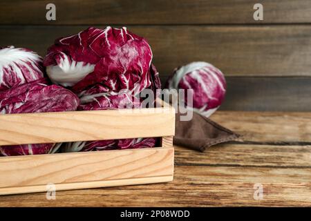 Fresh ripe radicchios in crate on wooden table, space for text Stock Photo