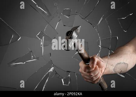 Man breaking window with hammer on dark grey background, closeup Stock Photo