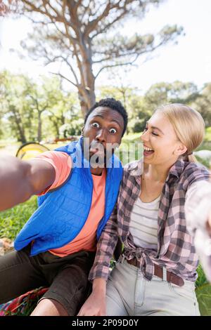 Vertical of happy, diverse couple having fun taking selfie in countryside, copy space Stock Photo