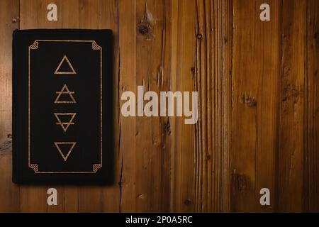 Close-up on black Alchemy book with a gilded Four Elements (Fire, Air, Earth and Water) in its middle. Stock Photo
