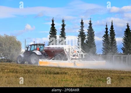 Tractor and spreader spreading agricultural lime, a soil additive made from pulverized limestone or chalk, onto stubble field on a day of autumn. Stock Photo