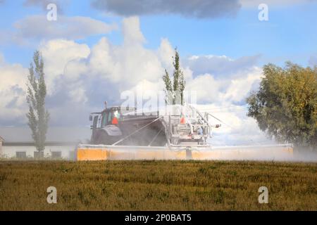 Tractor and spreader spreading agricultural lime, a soil additive made from pulverized limestone or chalk, in field on a day of autumn. Rear view. Stock Photo