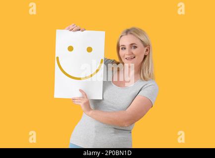 Woman holding paper with happy emoticon on yellow background Stock Photo