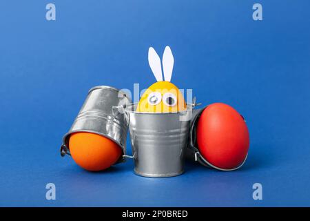 Funny Easter eggs in buckets on blue background Stock Photo