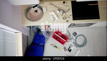High Angle View Of Male Plumber In Overall Fixing Sink Pipe Stock Photo