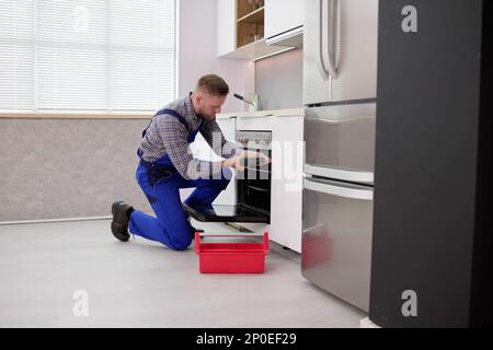 Young Man In Overall Repairing Washing Machine Stock Photo