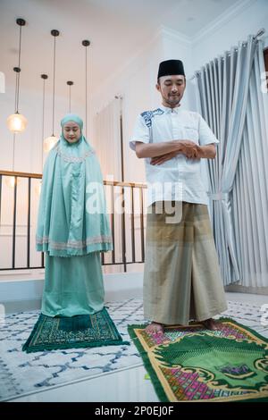 Asian man leads prayer with woman during Surah Al-Fatihah movement Stock Photo