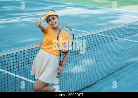 Beautiful tennis player woman with thumbs up while holding racket Stock Photo