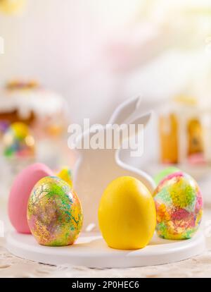 Easter composition with colorful Easter eggs on rabbit dessert plate. Traditional Easter treat on festive table decorated with spring flowers. Stock Photo