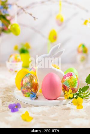 Easter composition with colorful Easter eggs on rabbit dessert plate. Traditional Easter treat on festive table decorated with spring flowers. Stock Photo