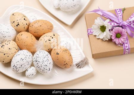 Easter eggs and flowers on plate and gift box over beige background Stock Photo