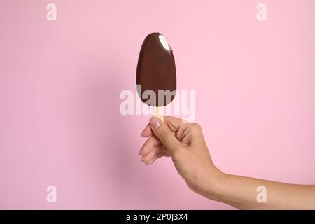 Woman holding bitten ice cream glazed in chocolate on pink background, closeup Stock Photo