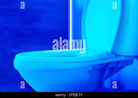 Toilet bowl in public restroom lit with UV blue light, closeup view Stock Photo