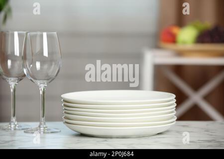 Stack of plates and glasses on white marble table indoors Stock Photo
