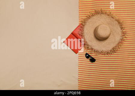 Striped beach towel, hat, open book and sunglasses on sand, top view. Space for text Stock Photo