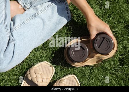 Woman holding takeaway cardboard coffee cups with plastic lids on green grass, top view Stock Photo