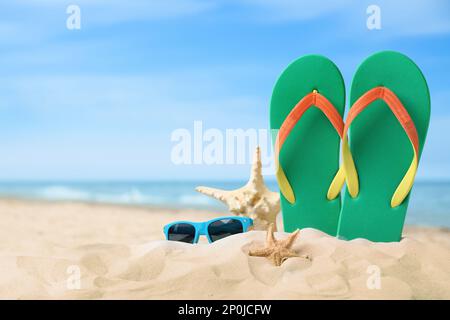 Green flip flops, starfishes and sunglasses on sand against white ...