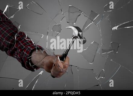 Man breaking window with hammer on dark grey background, closeup Stock Photo