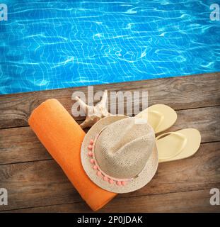 Beach towel, flip flops, straw hat and starfish on wooden surface near swimming pool, flat lay Stock Photo