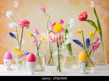 Beautiful flowers bouquets in glass vases on festive Easter table. Colored Easter eggs in egg cups Stock Photo