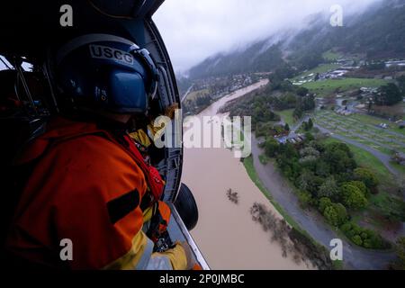 Petty Officer 3rd Class Clayton Maidlow, an Aviation Survival Technician stationed at Coast Guard Air Station Astoria, surveys a flooded region of the Russian River during an overflight mission on January 11, 2023. U.S. Coast Guard aircrews deployed to the San francisco Bay Area from across the west coast in response to the recent flooding. Stock Photo