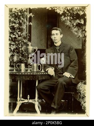 Original Victorian photograph of gent, on a table there is displayed a large Worcester challenge vase, / regatta trophy for rowing, and other cups,  Possibly member of a coxed four crew. Worcester area, U.K.  circa 1897-1899 Stock Photo