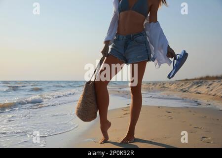Woman with beach slippers and bag on sandy seashore, closeup Stock Photo