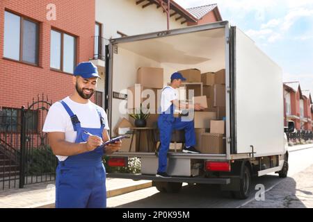 Moving service workers outdoors, unloading boxes and checking list Stock Photo