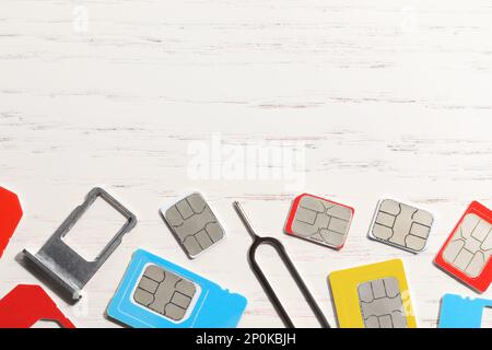 Different SIM cards, ejector and tray on  white wooden background, flat lay. Space for text Stock Photo