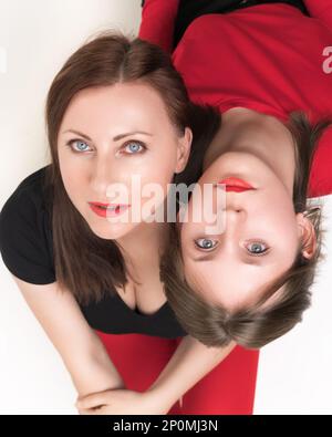 High angle shot of mother and teenager daughter sitting with their backs to each other, put their heads on each other's shoulders. Both females lookin Stock Photo