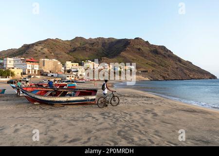 Local teenager with a bicycle near traditional wooden fishing boat looking at the Sao pedro sandy beach on Sao Vicente island, Cabo verde Stock Photo