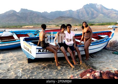 Local teenagers relaxing on a traditional wooden fishing boat on beautiful sao pedro sandy beach on Sao vicente island, Cabo verde Stock Photo