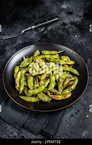 Stir-fried green Edamame Soy Beans with sea salt and sesame seeds in a plate. Black background. Top view. Stock Photo