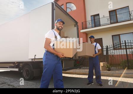 Workers unloading boxes from van outdoors. Moving service Stock Photo