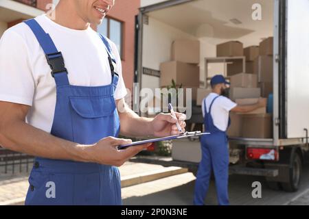 Moving service workers outdoors, unloading boxes and checking list Stock Photo