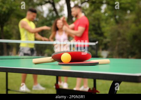 Friends talking near ping pong table outdoors, focus on rackets and ball Stock Photo
