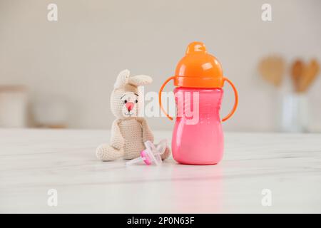 Baby bottle, toy and pacifier on white marble table indoors. Maternity leave concept Stock Photo
