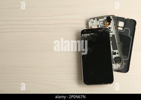 Parts of broken smartphone on white wooden table, flat lay with space for text. Device repair Stock Photo