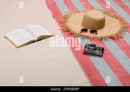 Beach towel, hat, sunglasses, camera and open book on sand Stock Photo