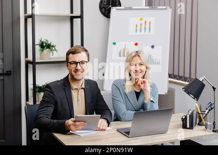 Start up business team on meeting in modern office interior, working on laptop and tablet. A young woman and a man are sitting at the table and workin Stock Photo